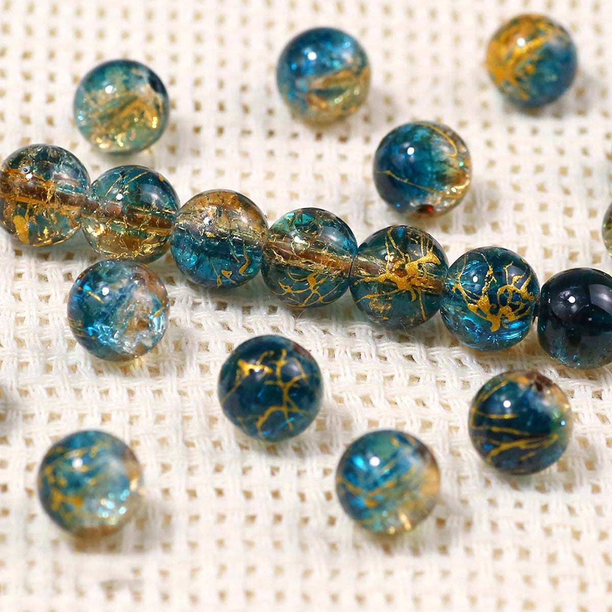 A collection of blue and gold gradient crystal glass beads with a crackle finish scattered on a white textured surface.