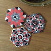 Three geometric mosaic patterns made from small fuse beads in pink, black, and gray on a wooden surface.