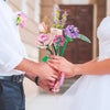 A bride and groom are holding a colorful floral bouquet made from building blocks for a wedding display.