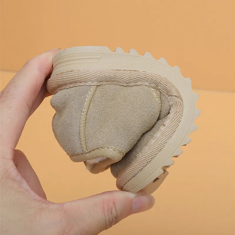 A hand holds a tan cozy leather winter boot for toddlers with an anti-slip rubber sole.