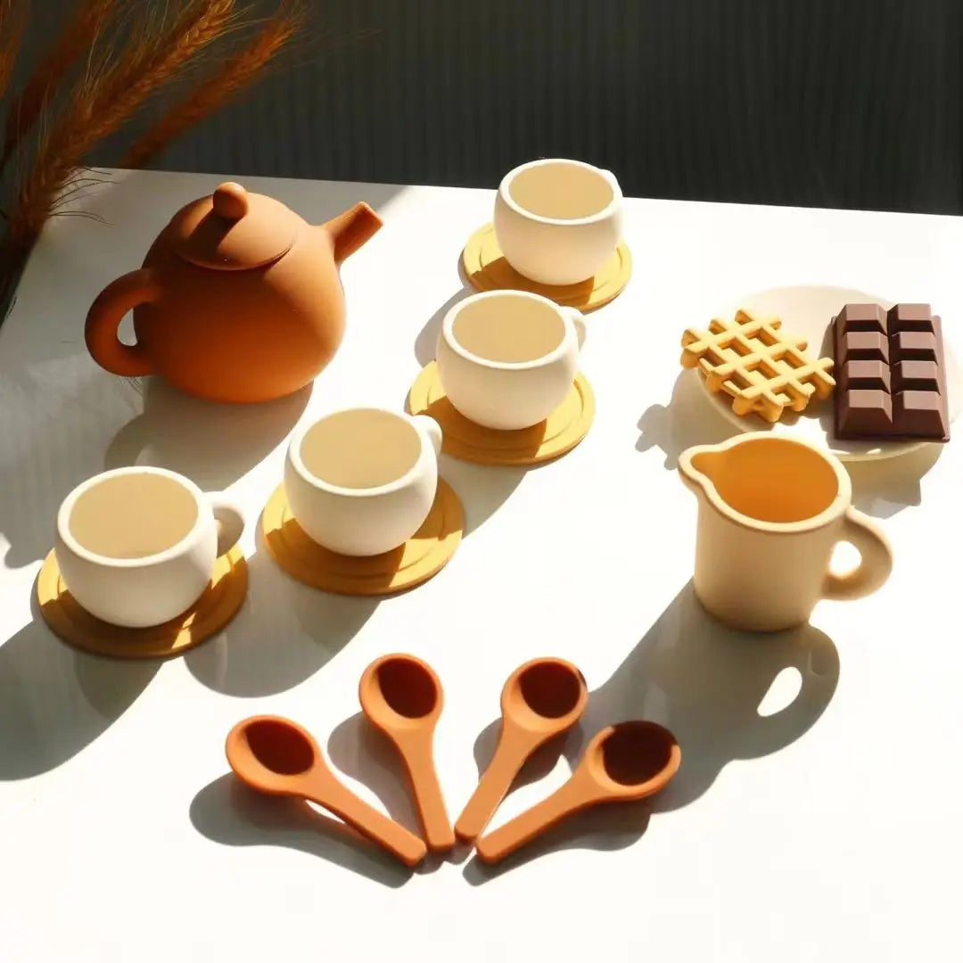 An orange silicone pretend play tea set featuring a teapot, cups, and food items on a white surface.