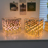 Two clear glass cubes filled with glowing pink and yellow tulip lights displayed on a white shelf.