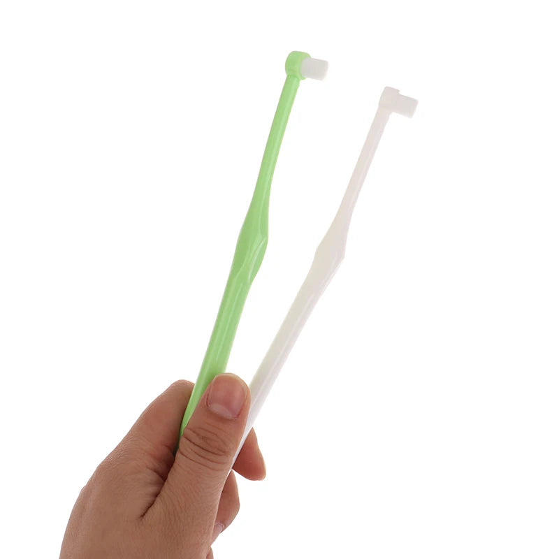 A hand holds a pair of orthodontic interdental brushes, one green and one white.