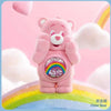 A pink Care Bear figurine with a rainbow belly is shown against a light pink background.