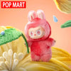 A red Labubu plush doll with pink ears is displayed on a yellow textured surface.