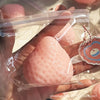 A hand holds a pink strawberry squishy fidget toy sealed in a clear plastic bag.