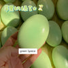 A hand holds a green squishy cheese cake stress relief toy, showing one piece of the product.