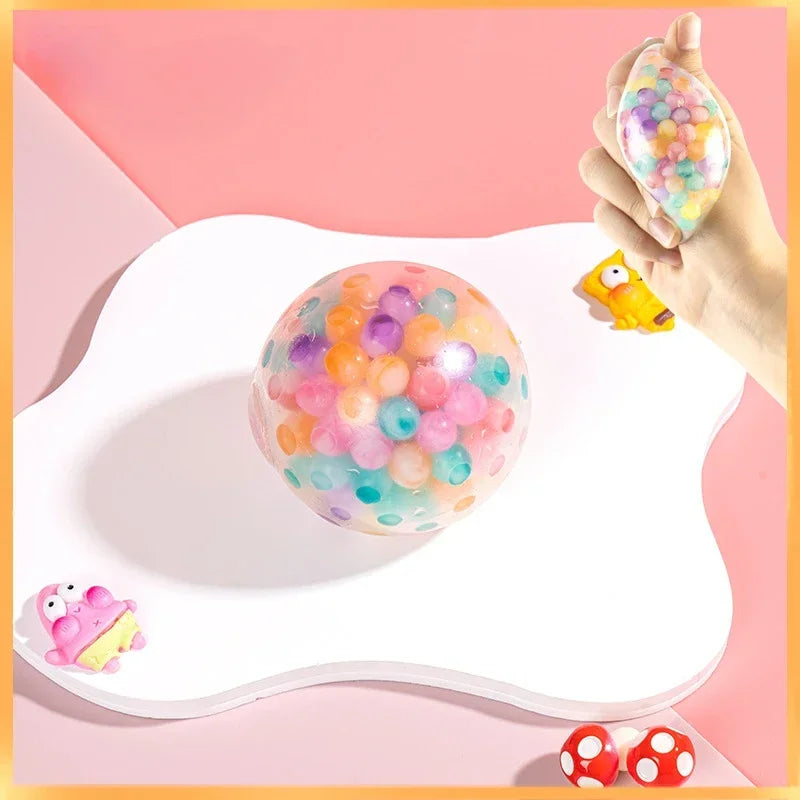 A hand holds a colorful, translucent pressure reducing fidget squishy ball on a white surface.
