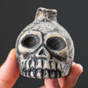 A ceramic Aztec skull whistle with detailed facial features is held in a hand against a dark background.