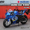 A blue Suzuki GSX-R1000 motorcycle model in 1:18 scale displayed against a red industrial background.