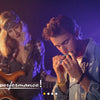 Three musicians performing with a harmonica and guitar under stage lights.