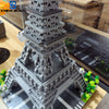A detailed miniature model of the Eiffel Tower built from gray LEGO-style blocks on a black and white grid surface.