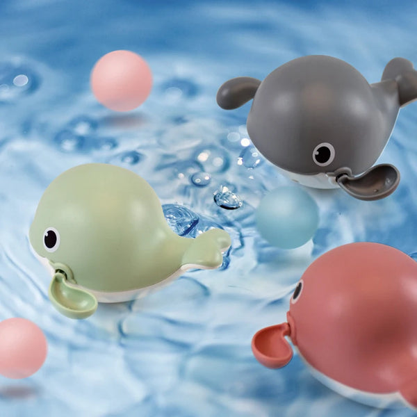 Trois jouets de bain en silicone en forme de créatures marines roses, vertes et grises flottant dans l'eau claire.