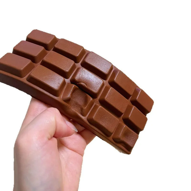 A hand holds a realistic brown chocolate squishy toy with a waffle pattern.