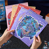 A hand holds a stack of colorful 3D cartoon scene stickers for scrapbooking and journaling.