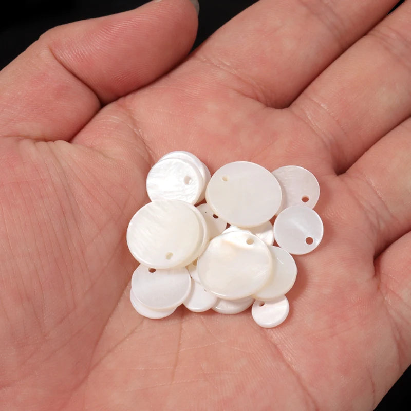 A handful of natural white shell beads in various round sizes is held in a person's hand.