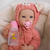 A realistic silicone reborn baby doll wearing a pink knitted animal hood and holding a pink bottle.