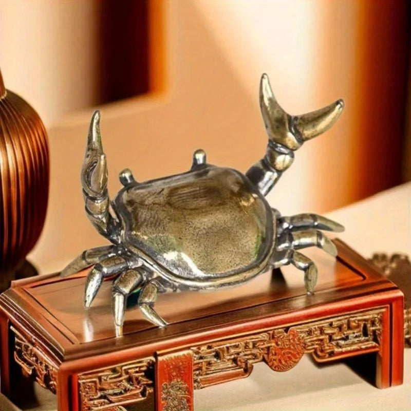 A brass crab figurine statue resting on a wooden box.