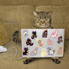 A tabby cat is looking at a laptop featuring a pack of cute cartoon cat stickers.