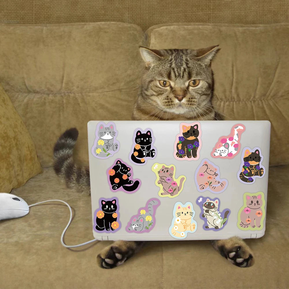 A tabby cat is looking at a laptop featuring a pack of cute cartoon cat stickers.