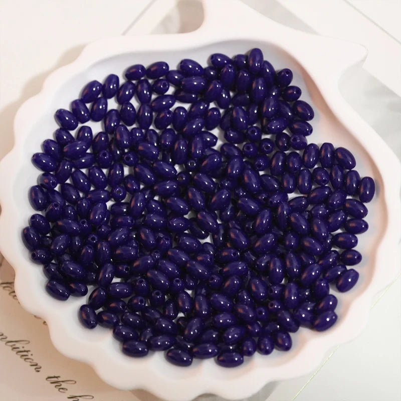 A pile of dark purple oval glass rice grain beads for jewelry making in a white dish.
