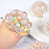 A hand holds a cluster of colorful, translucent stress relief balls with mesh netting on a white surface.