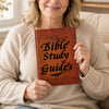 A woman holds a brown Bible study guide book against her sweater.