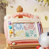 A pink magnetic drawing board for kids is shown on a wooden table with scattered leaves.