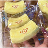 A yellow banana shaped squishy stress relief toy with a bear face design is shown in clear plastic packaging.
