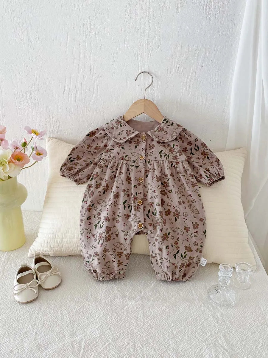 A floral print baby girl jumpsuit with a doll collar and long sleeves is displayed on a white surface.