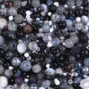 A close-up view of a vibrant glass bead mix featuring various sizes and shades of black, gray, purple, and iridescent beads.