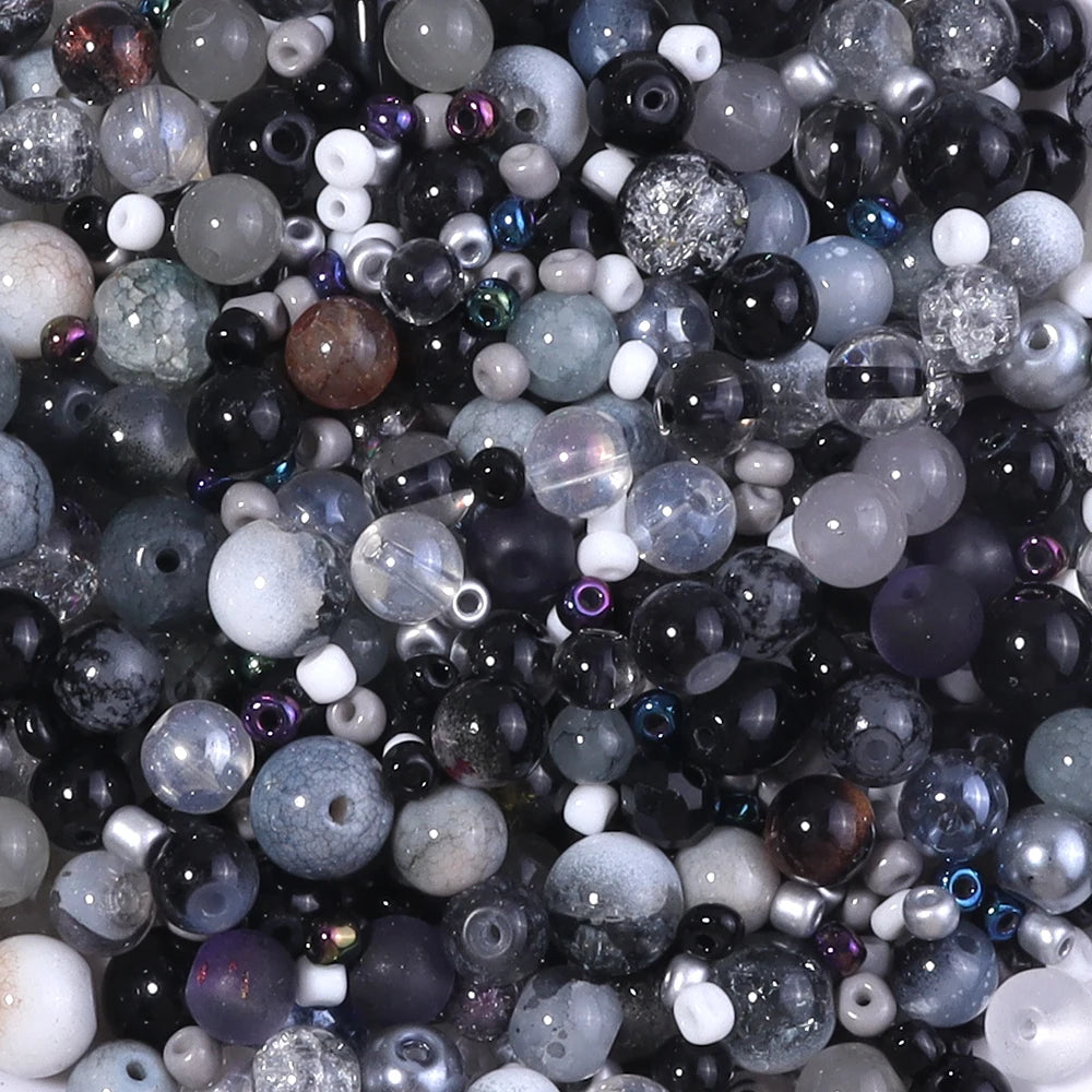 A close-up view of a vibrant glass bead mix featuring various sizes and shades of black, gray, purple, and iridescent beads.
