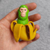 A hand holds a green monkey figure and a yellow stick figure set of wooden toys.