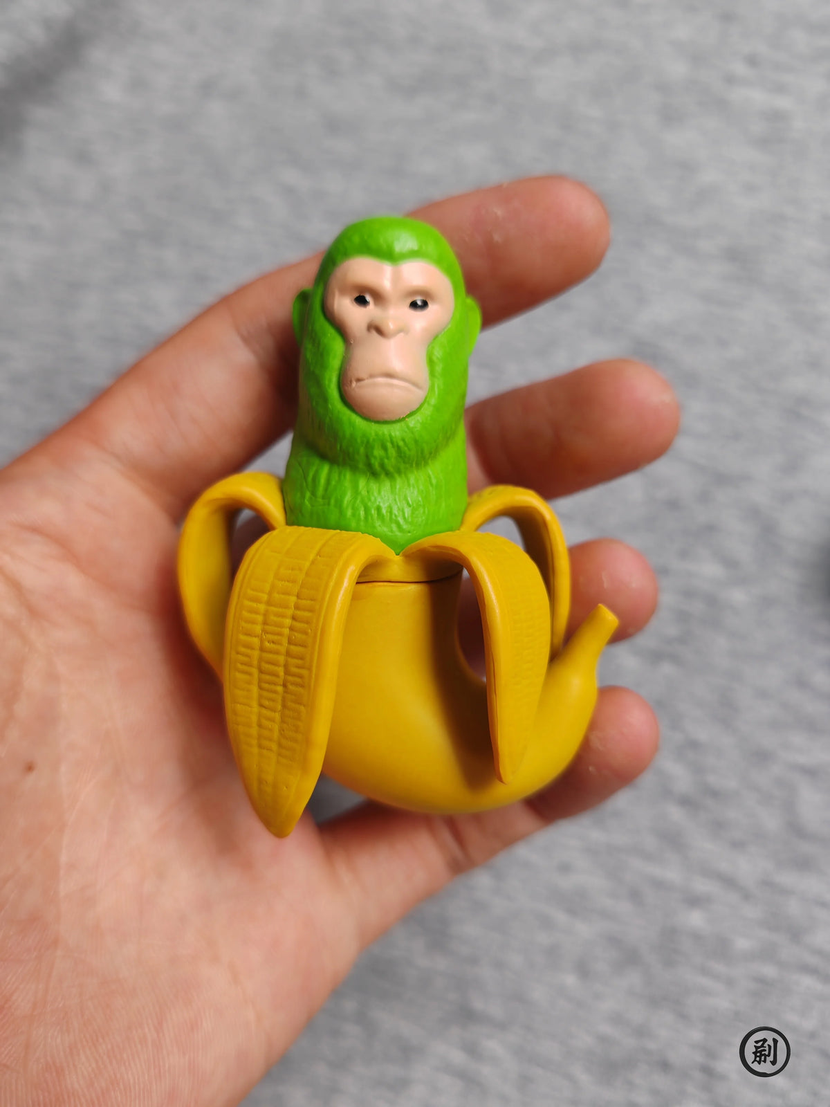 A hand holds a green monkey figure and a yellow stick figure set of wooden toys.