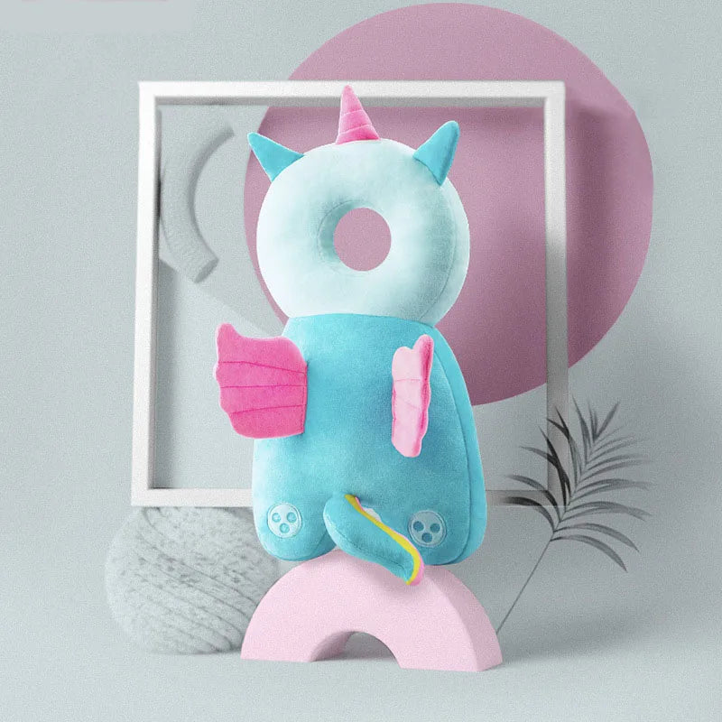 A light blue plush baby head protector pillow with pink accents and adjustable straps, set against a soft pink background.