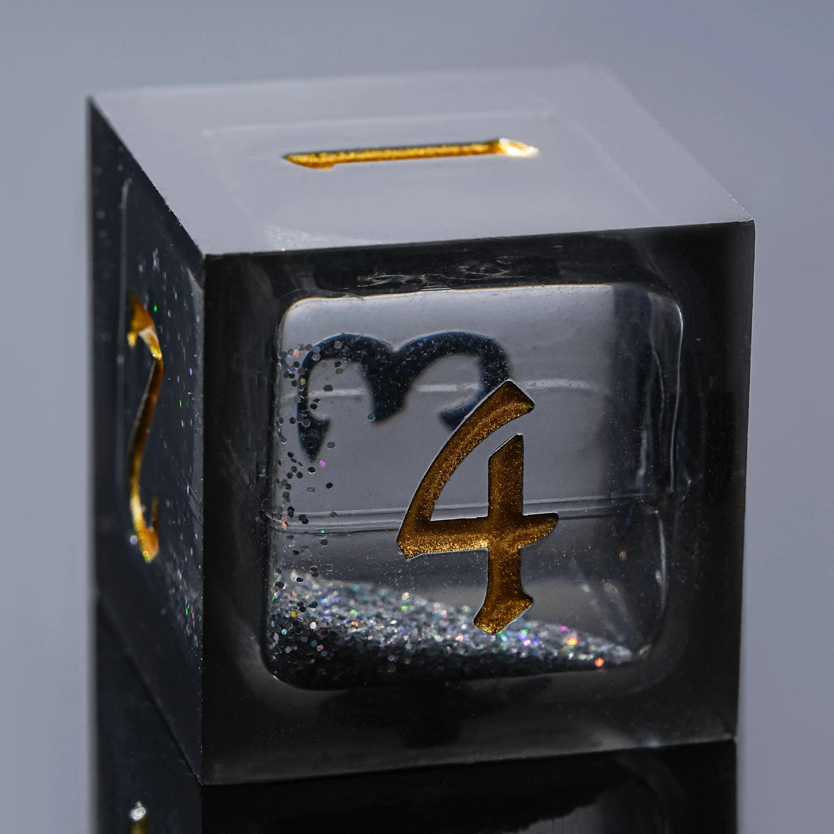 A close-up view of a black liquid core resin dice set featuring a four-sided die with gold lettering.