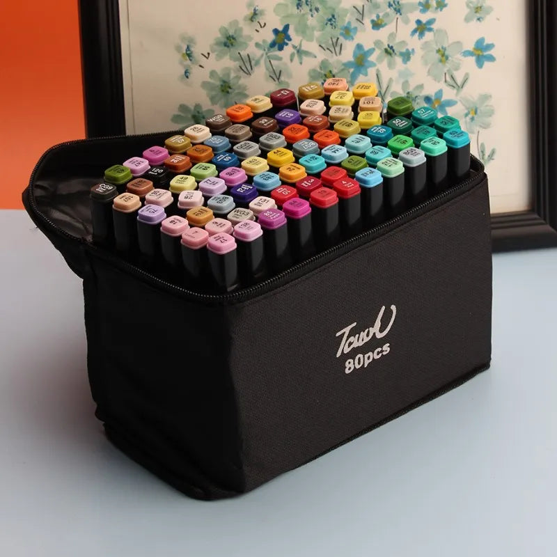 A black case filled with alcohol art markers featuring various colors and tips, displayed in front of a framed floral print.