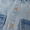 Close-up of a blue and white striped denim jacket featuring brass buttons and visible stitching details.