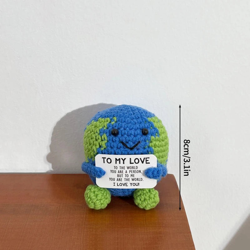A handmade crochet pocket hug doll shaped like the Earth, colored green and blue, with a tag that reads I love you to the wor