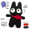 A black crocheted animal figure with large eyes and a red accessory, shown next to yarn and a DIY instruction sheet.
