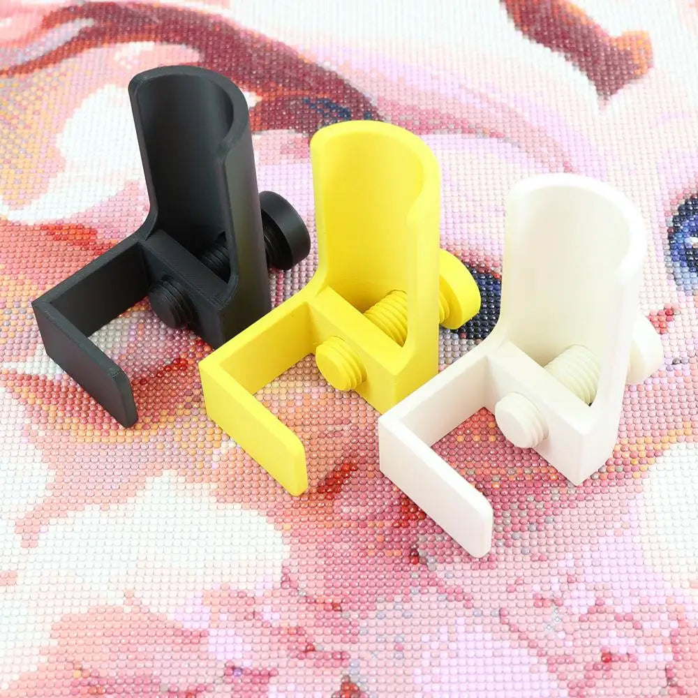 Three adjustable diamond painting canvas stands in black, yellow, and white are displayed on a pink patterned surface.