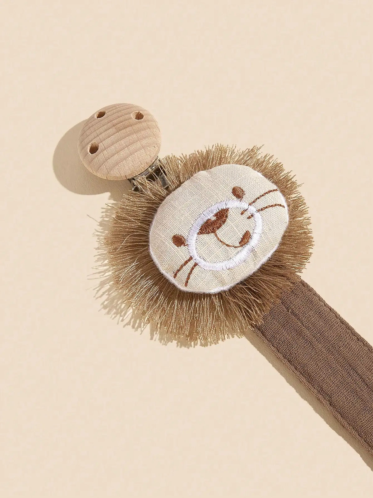 A beige elephant pacifier holder featuring a felt elephant head and a wooden clip on a brown strap.