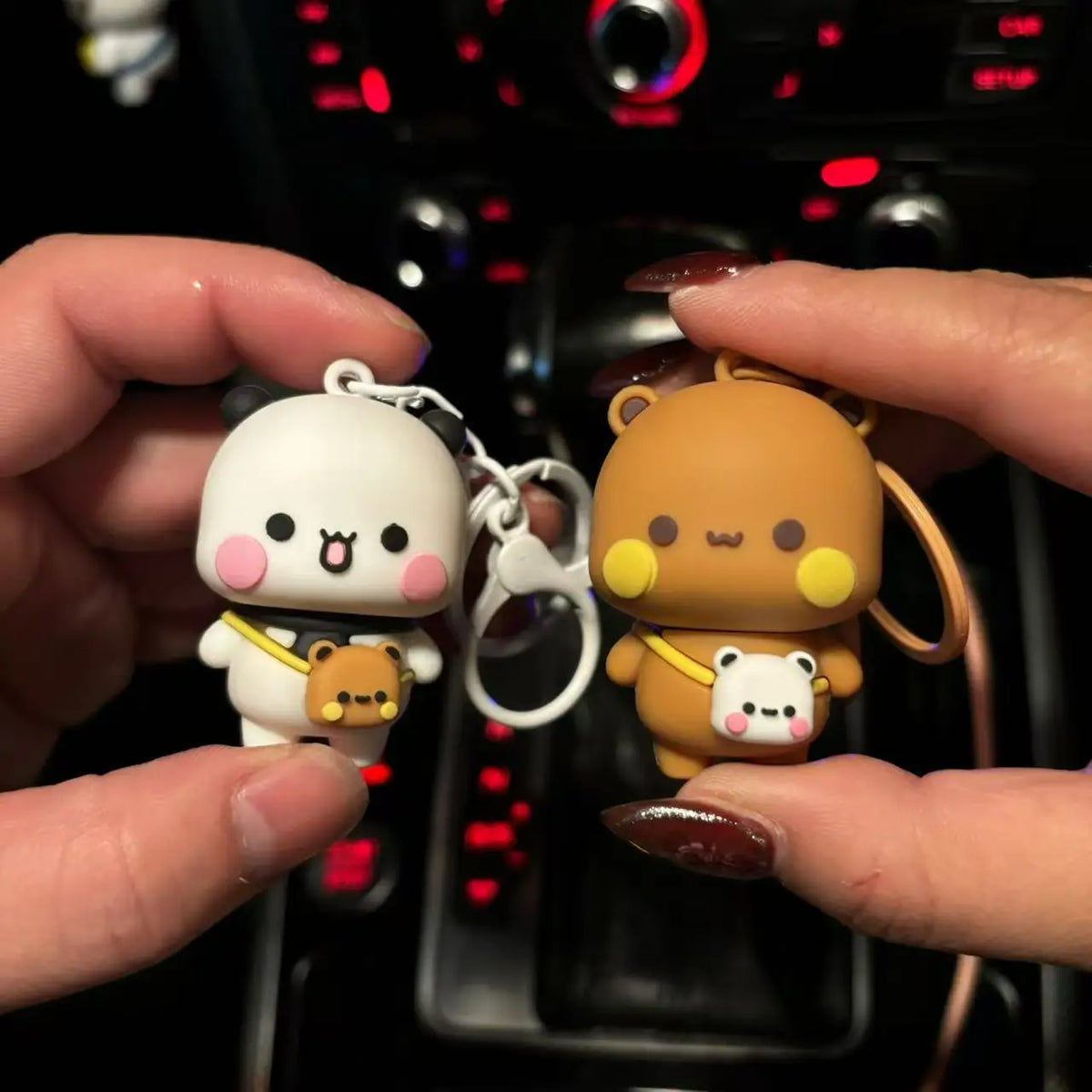 A pair of cute cartoon bear keychains, one white and one brown, being held against a dark background.