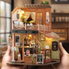 A wooden miniature dollhouse kit featuring a coffee shop facade with detailed furniture and LED lighting.