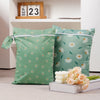 Two reusable waterproof baby wet bags with a light green background and white daisy pattern are displayed on a white box.