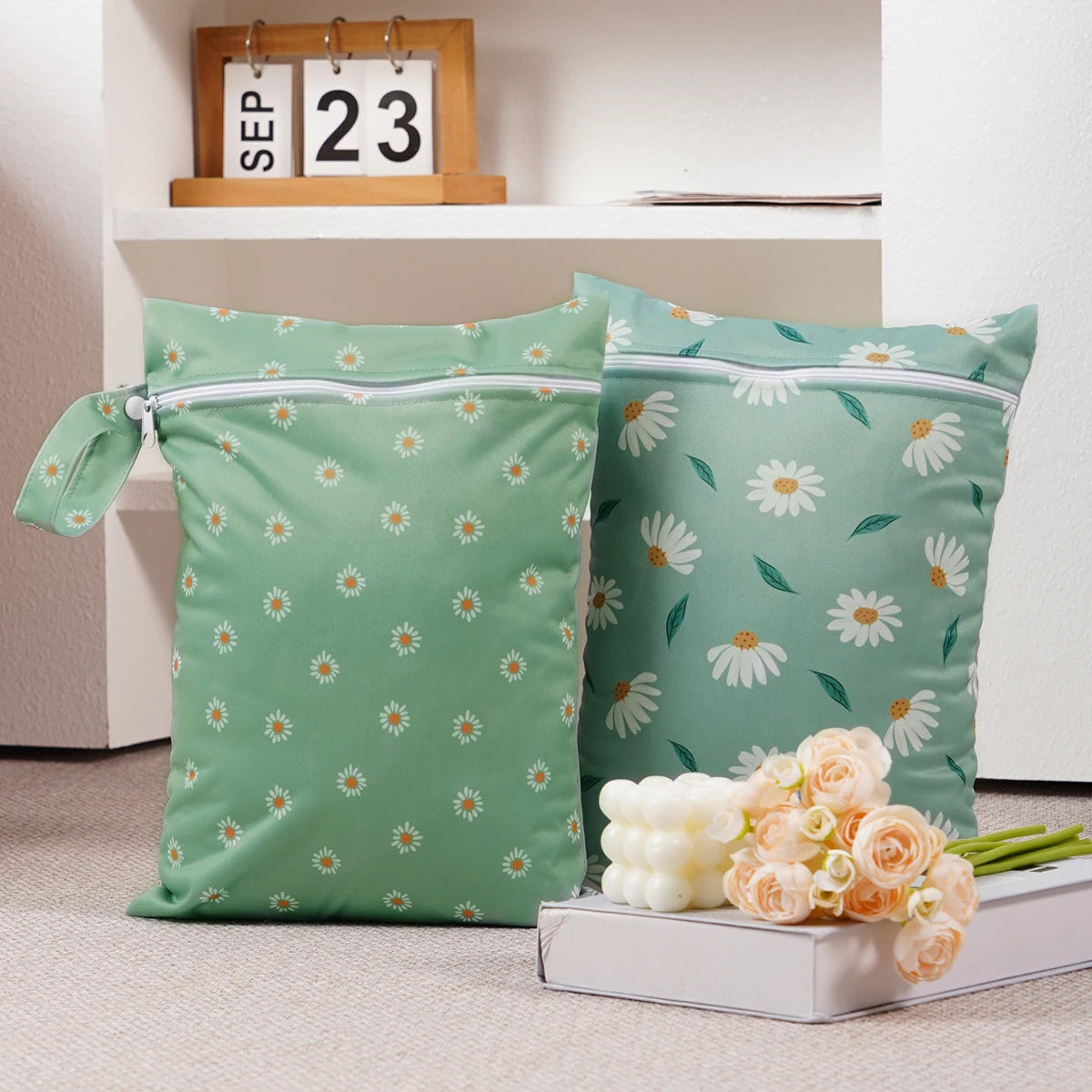 Two reusable waterproof baby wet bags with a light green background and white daisy pattern are displayed on a white box.