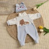 A white baby romper featuring cute brown teddy bears and a matching knitted hat, displayed on a woven mat.