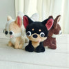 Three plush dog dolls, including a black Chihuahua with tongue out, are displayed on a white surface.
