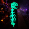 A glowing green dinosaur skeleton mask stands in a dark outdoor setting with Halloween lights and fog.