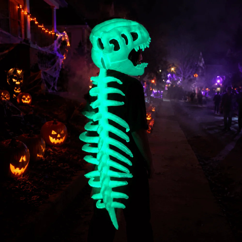 A glowing green dinosaur skeleton mask stands in a dark outdoor setting with Halloween lights and fog.